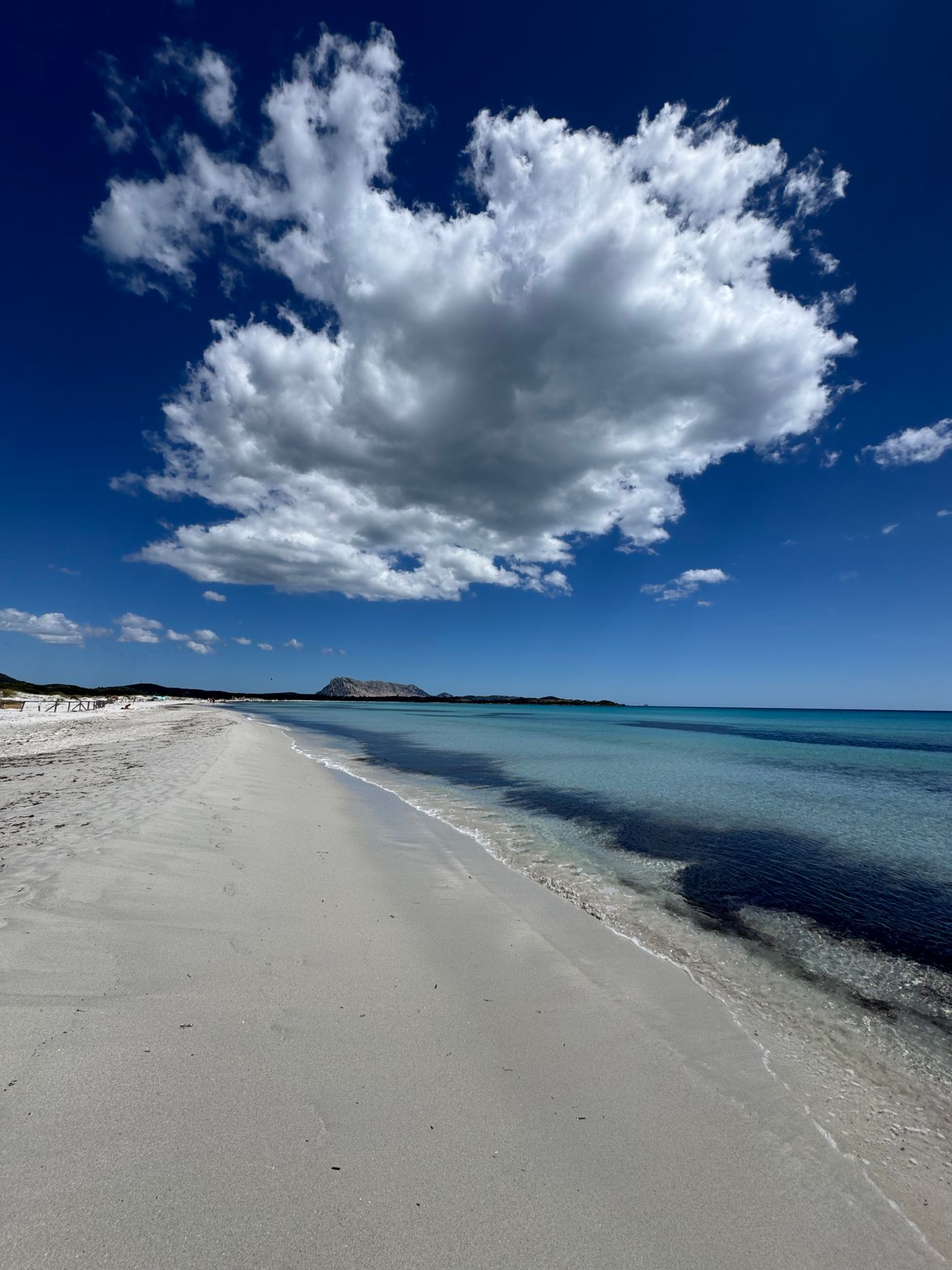 A wide Sardinian beach under dramatic summer clouds